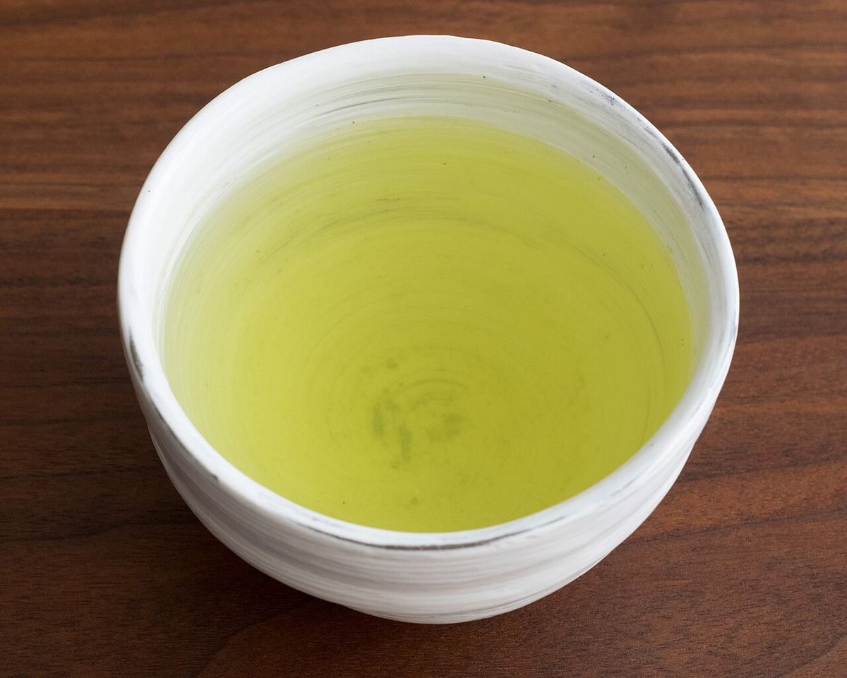 Porcelánová miska se světle zeleným nálevem senchy na dřevěném stole