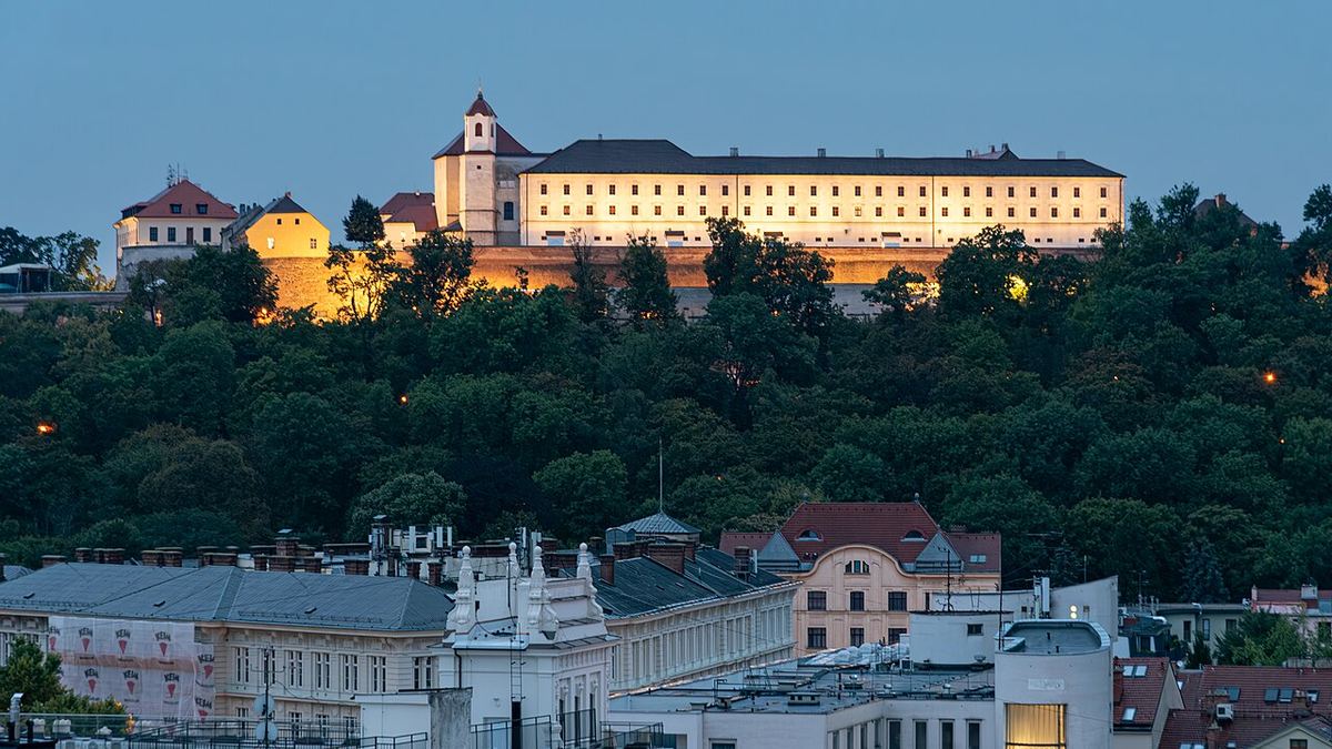 Hrad Špilberk na zalesněném kopci nad Brnem ve večerním osvětlení